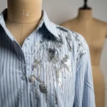 Elegant light blue and white vertical pinstripe women's formal shirt featuring premium silver sequin floral embroidery on the left shoulder (3)