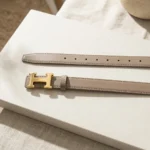 Slim taupe leather women's belt with gold H motif buckle, premium fashion accessory (2)