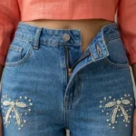 Women's high waisted blue jeans featuring white pearl and rhinestone bow patterns on the front legs (3)