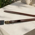 Women's smooth brown leather belt with antique gold CD monogram buckle on a stone surface (1)