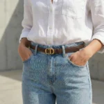 Women's smooth brown leather belt with antique gold CD monogram buckle on a stone surface