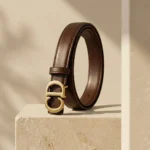Women's smooth brown leather belt with antique gold CD monogram buckle on a stone surface (2)