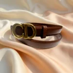 Women's smooth brown leather belt with antique gold CD monogram buckle on a stone surface (3)