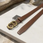 Women's smooth brown leather belt with antique gold CD monogram buckle on a stone surface (5)