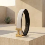 a white textured leather belt with a gold H shaped buckle (1)