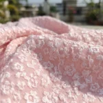 Elegant light pink mini dress for women featuring 3D floral texture, sheer high neck with ruffles, and a bow back detail (3)