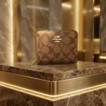 brown Coach Signature Canvas Micro Wallet in a cafe setting; close up of Coach micro zip wallet with gold logo (1)