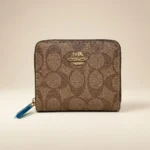 brown Coach Signature Canvas Micro Wallet in a cafe setting; close up of Coach micro zip wallet with gold logo (2)