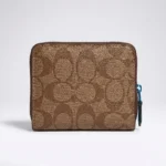 brown Coach Signature Canvas Micro Wallet in a cafe setting; close up of Coach micro zip wallet with gold logo (3)