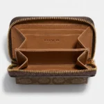 brown Coach Signature Canvas Micro Wallet in a cafe setting; close up of Coach micro zip wallet with gold logo (4)